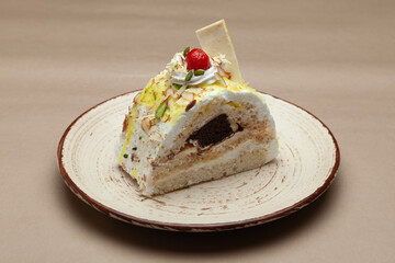 A piece of Delicious pastry with shredded dry fruits and cherry on top. On a white plate. Front view.