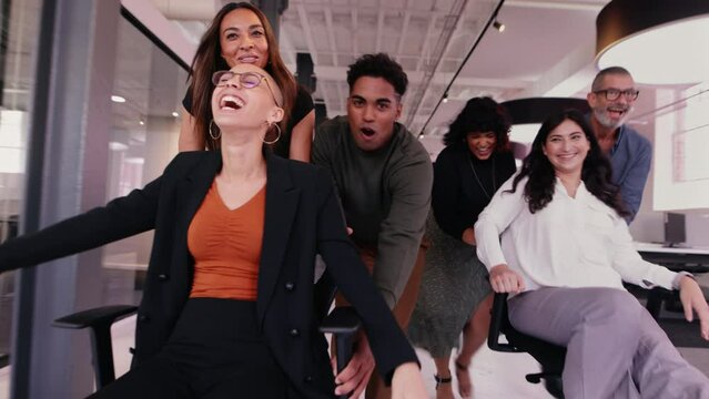 Business people having fun in an office, pushing each other on swivel chairs on a playful work break. Group of successful business professionals taking a moment to celebrate after completing a project