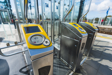 Outdoor entrance to the railway station through stainless-steel yellow ticket barrier. Modern...
