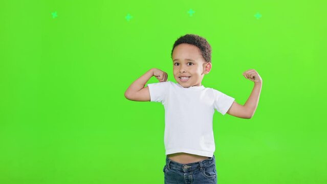 Little african american boy demonstrating strength, while raising arms indoors. Front view of funny little power super hero kid showing muscles, isolated on green studio background. Concept of power.