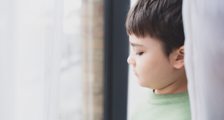 Portrait Kid Boy, Side view School Kid with sad face, Young boy looks out  behind the curtains on...