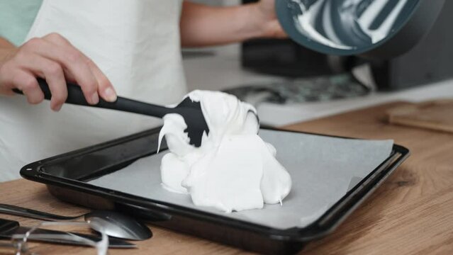 The pastry chef is piping meringue onto a baking sheet covered with parchment paper, in a close-up shot.