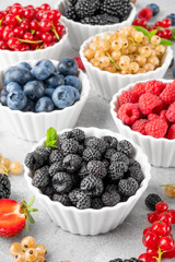 Various fresh berries in bowls on a gray concrete background. Healthy food concept.