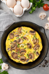 Omelette with mushrooms and herbs in a pan on a white wooden background. Healthy breakfast. Top view. Copy space.
