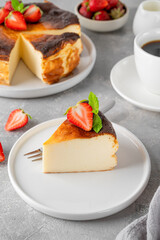 A piece of Basque burnt cheesecake or San Sebastian cheesecake with fresh strawberries on a white plate on a gray background. Selective focus. Copy space.