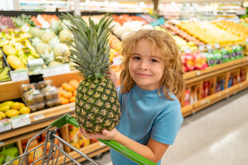 Cute child hold shopping cart full of groceries. Kid holds shopping basket. Store, shopping, sales and discounts. Little shopper. Kid holding shopping basket with organic vegetables and fruits.
