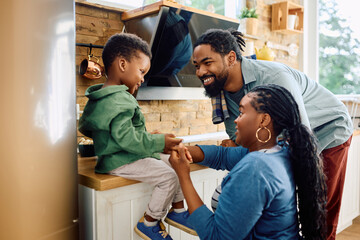 Happy black parents talk to their small son in kitchen.