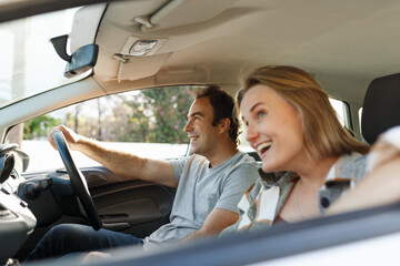 Emotional millennial couple having fun while car trip, listening to music and cheerfully singing, shot from inside the auto, sun flare