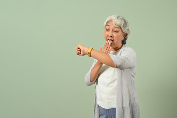 Shocked mature woman checking time on wrist watch isolated on light green background