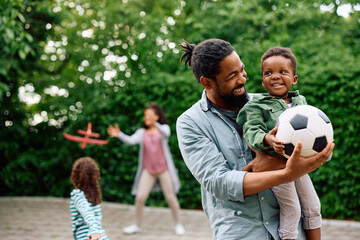 Happy black father and son with football in park.