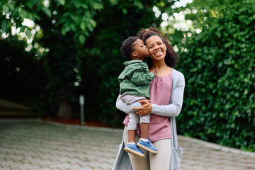 Small black boy kissing his mother outdoors.