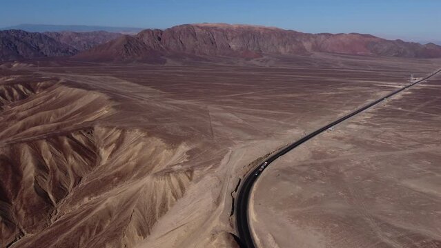 Aerial video of the desert plateau that holds the world famous Nazca Lines. Drone hovers high above and slowly turns camera right. Below is a highway and long linear geoglyphs and a spiral symbol.