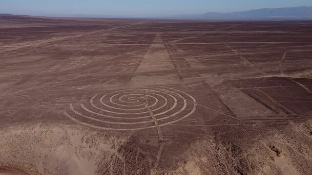 Aerial 4k video of the Nazca Lines. Drone flies backwards from a spiral ancient geoglyph. Desert plateau also filled with many long lines. Located in Nazca, Peru.