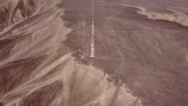 Aerial video of the Nazca Lines. Drone flies down while tilting camera up. Below in the desert plateau can be seen many linear geoglyphs and a depiction of a hummingbird. Located in Nazca, Peru.