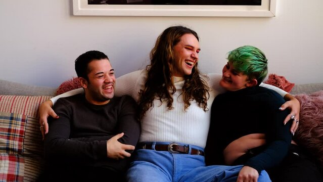 Friends having fun, laughing, sitting on sofa. Millennial transgender group enjoying friendship.