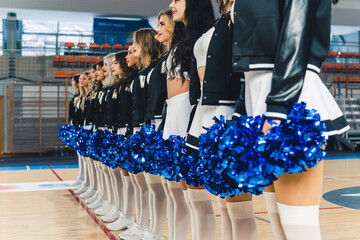 Cheerleaders young women standing in straight line with blue pompons on a court. High quality photo
