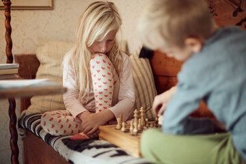 Little brother and sister playing chess together on a bed