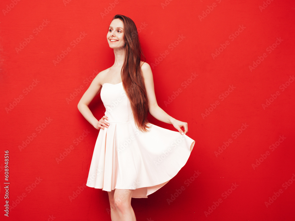 Wall mural Portrait of young winsome woman in romantic attire pretty smiling on red background. Slim female in pure pink dress posing in studio. Cheerful model. Isolated. Long hair