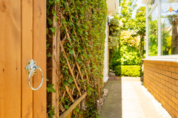 Shallow focus of a newly installed wooden garden gate. Showing the bright metal of the door handle, leading to a lush rear, enclosed garden.