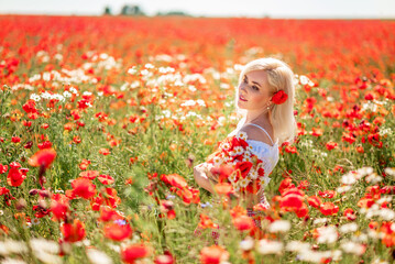 Portrait of a beautiful woman with a bouquet of daisies and poppies in a field with flowers. Red and white colors in clothing and flowering