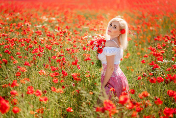 blonde woman in a poppy field with daisies. A girl with a bouquet of red and white flowers