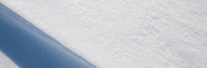 Beautiful winter background with snowy ground. Natural snow texture. Wind sculpted patterns on snow surface. Wide panoramic texture for background and design. Closeup top view with copy space.