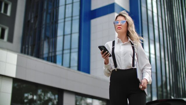 Businesswoman with smartphone standing on the central city street near modern office building