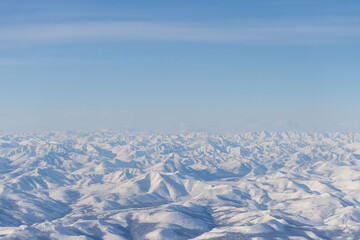 Fototapeta na wymiar Aerial view of snow-capped mountains. Winter snowy mountain landscape. Air travel to the far North of Russia. Kolyma Mountains, Magadan Region, Siberia, Russian Far East. Great for the background.