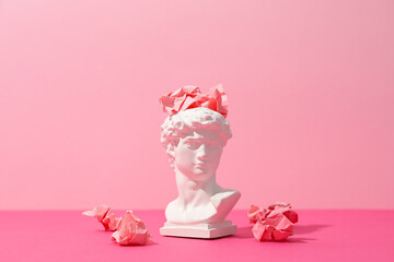 Ancient head with paper balls on pink background
