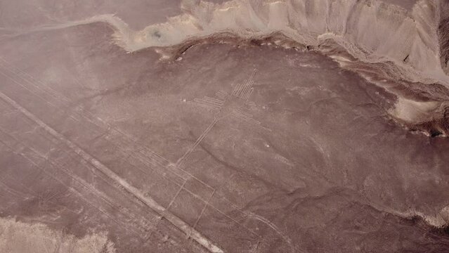 Ancient geoglyph of a hummingbird part of the famous Nazca Lines. Drone flies high above looking down. Some long long linear geoglyphs can also be seen. Located in desert plateau in Nazca, Peru.