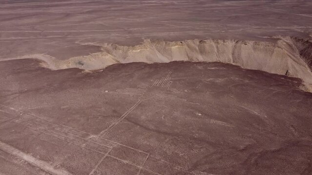 Ancient geoglyph depicting a hummingbird, part of the famous Nazca lines. Drone flies up while tilting camera down. Located in desert plateau in Nazca, Peru.