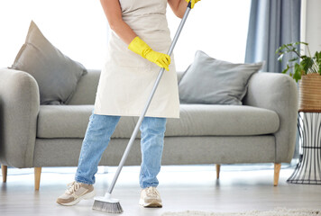 Cleaning, broom and sweeping with a housekeeper in the living room of a home for housework or chores. Floor, sweep and housekeeping with a cleaner in a house to tidy for hygiene during a spring clean