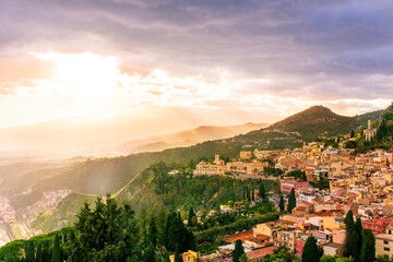 travel landscape of a highland mediterranean town with yellow buildings,  green trees and gardens, beautiful mountains and amazing cloudy sunset