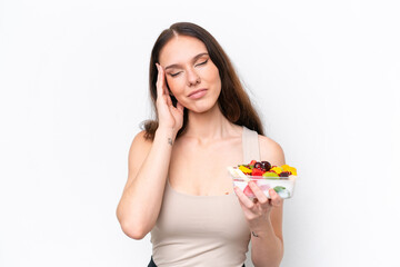 Young caucasian woman holding a bowl of fruit isolated on white background with headache