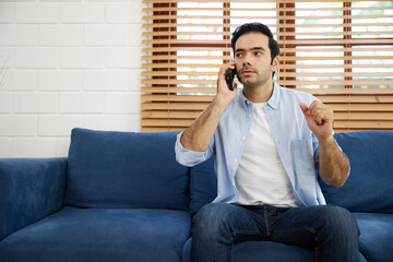 young handsome man sitting on sofa and talking by smartphone at home