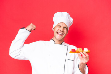 Young caucasian chef man holding sashimi isolated on red background celebrating a victory