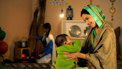 A village woman in a traditional Saree enjoys cuddling and playing with her small daughter -...