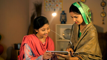 A young girl and her middle-aged mother watching an online video on a tablet - village home  entertainment  digital device. A modern village family using a tablet together - social media  internet ...
