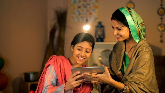 An Indian housewife and her young daughter making a video call on a tablet - digital device  modern technology  village home. Modern villagers wave hands happily while talking online - distant comm...