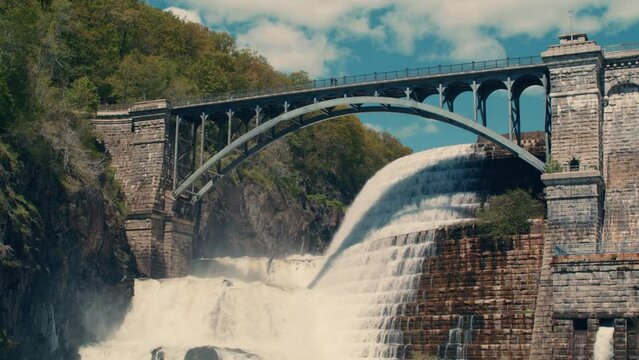 wide shot of bridge at the top of new croton dam with stepped spillway, trees and blue sky in the background. Slow motion 40fps. static.