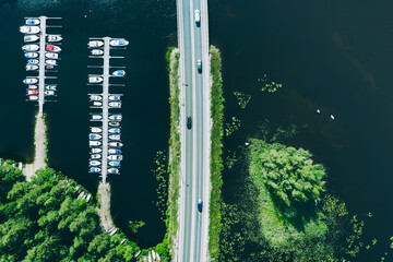 Obraz premium Aerial view of road with cars between green forests and blue lakes with marina boats in Finland