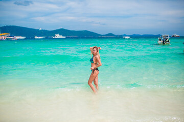 A young happy girl with a beautiful figure is standing in a bathing suit on the beach of an exotic island by the sea, a luxury resort, a concept of relaxation, vacation on a tropical beach in Thailand