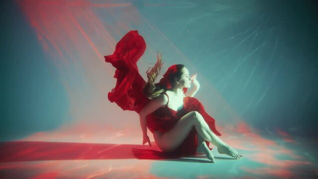 Sexy girl fashion model posing underwater dive for creative photo video shooting waving long legs hands. Fantasy queen woman swims in dark water neon light. silk long red dress. aqua studio pool 4k