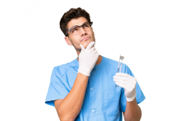 Young dentist man holding tools over isolated background having doubts