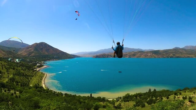 paragliding in Uzbekistan. back view from gopro man paraglider flying over the Amirsoy ski slope and Charvak lake. Extreme and active types of recreation. High quality FullHD footage