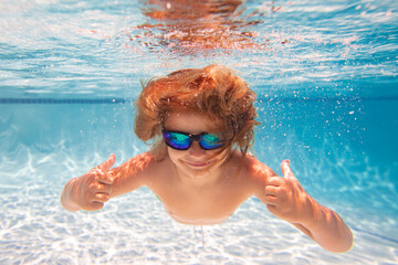 Naklejka premium Child in swimming in pool. Funny little boy swims underwater in the pool. Underwater kids portrait from under the water. Summer holiday. Kids weekend.