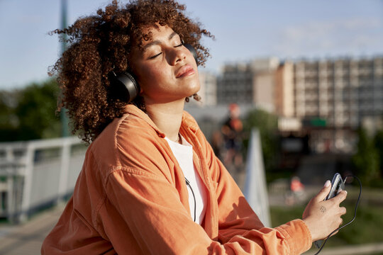 Black woman wearing headphones and listening to music during the sunset