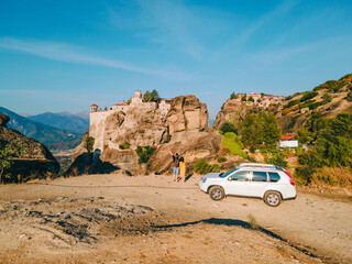 couple standing near car looking at meteora monastery Thessaly mountains Greece