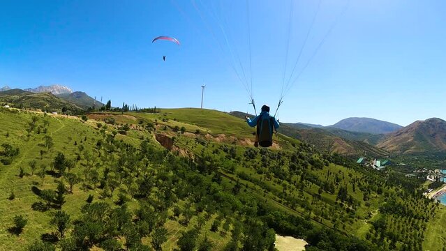 paragliding in Uzbekistan. back view from gopro man paraglider flying over the Amirsoy ski slope and Charvak lake. Extreme and active types of recreation. High quality FullHD footage