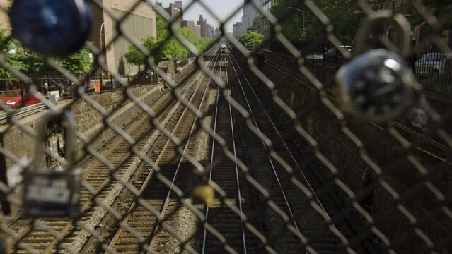 New York City Trains Pass Under Street On Upper East Side Of Manhattan, With Padlocks Hanging On Fence In Foreground